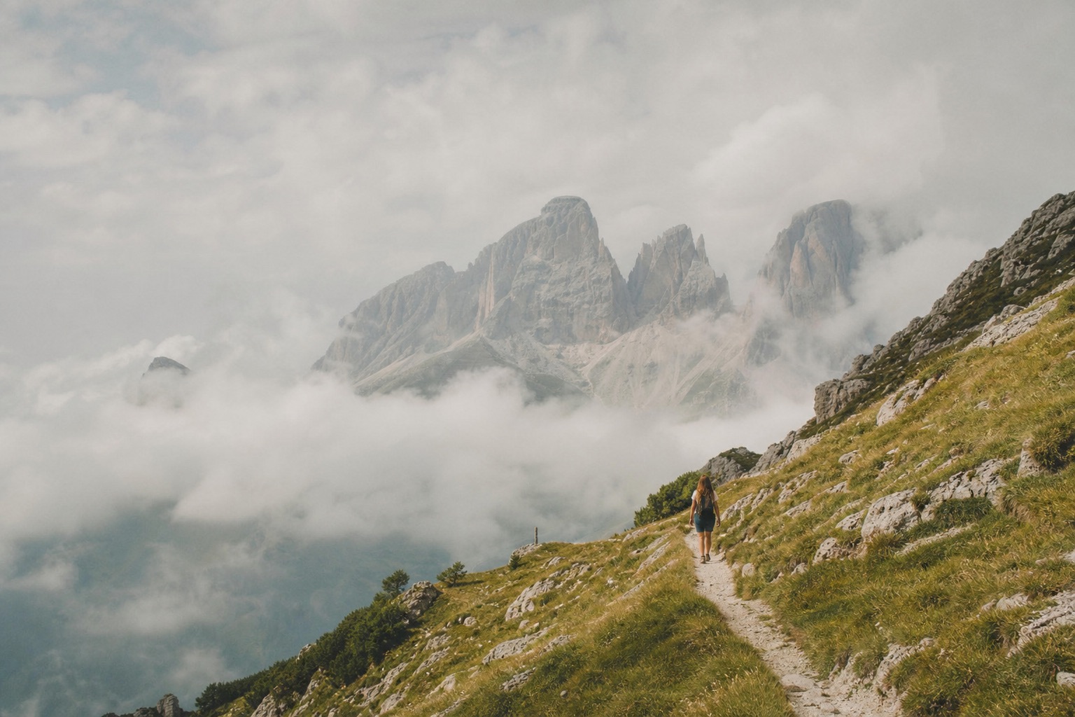 A lone hiker on a mountain trail above clouds in the Dolomites