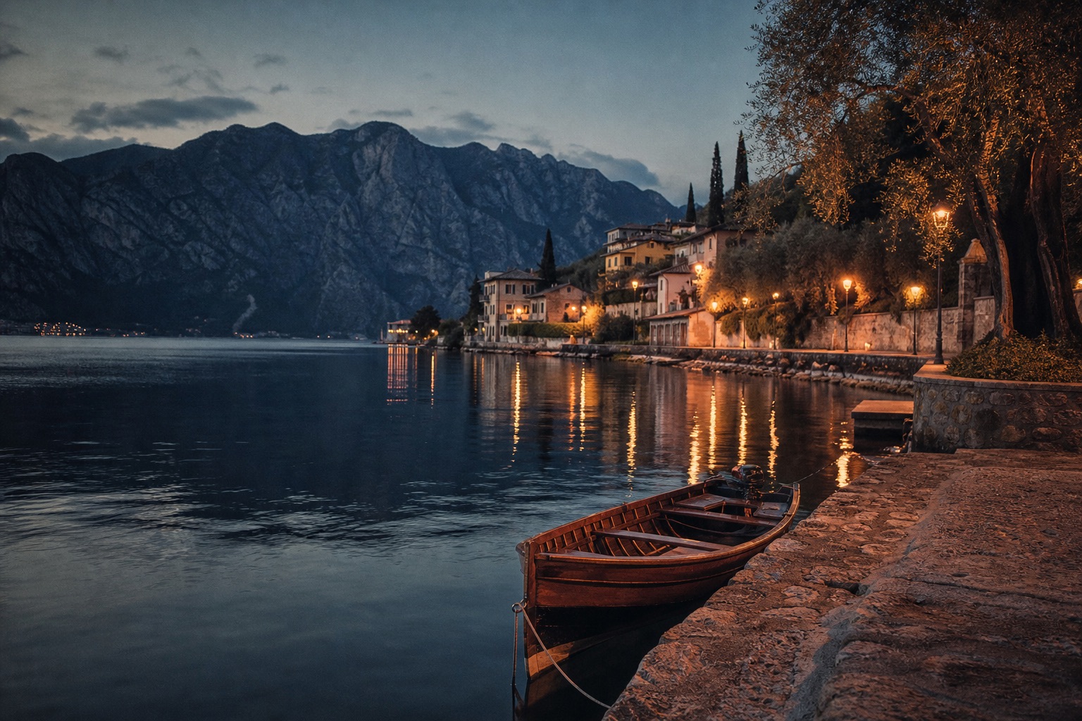 A wooden boat beside a quiet stone waterfront at Lake Garda after sunset